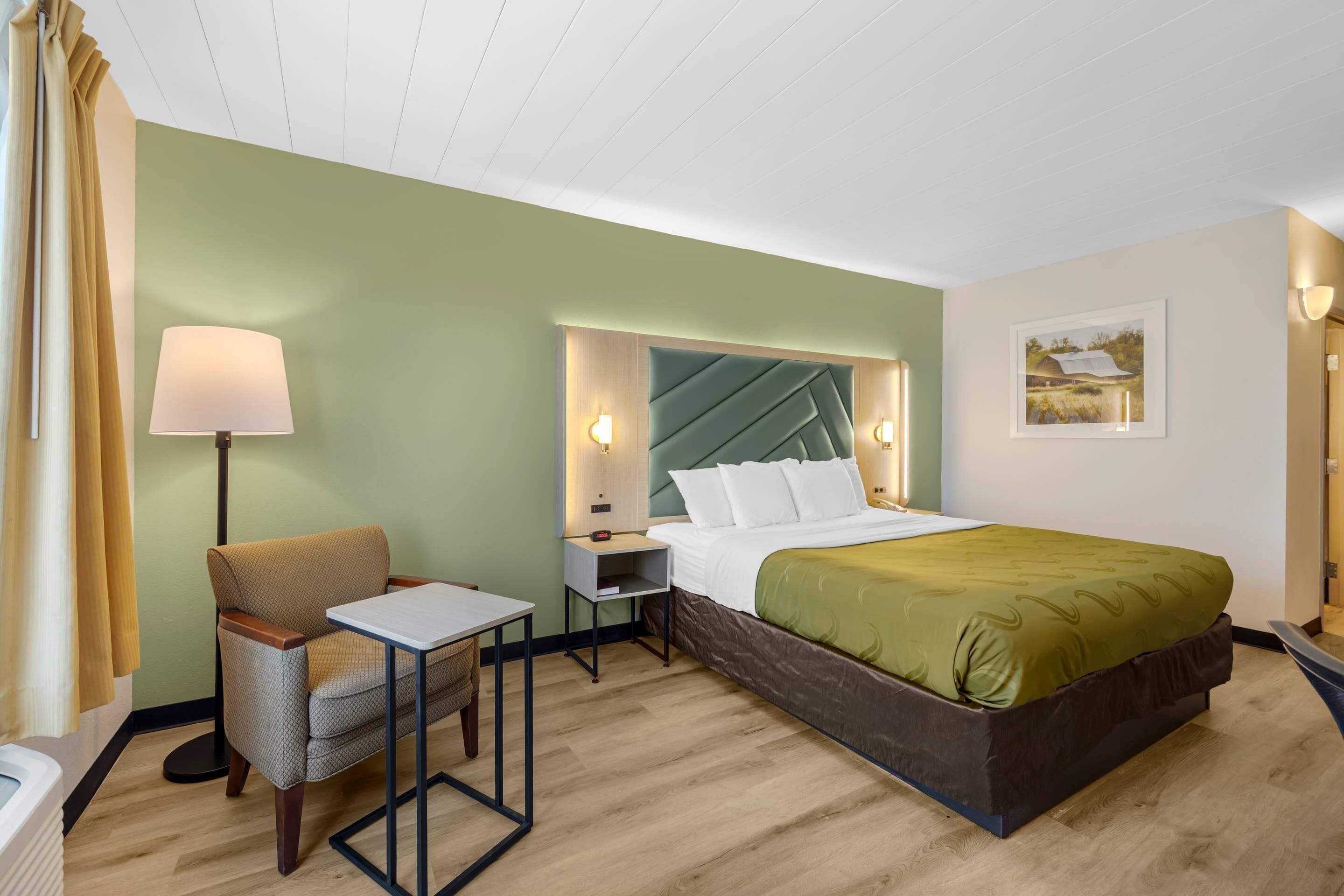 Una habitación de hotel con cama, escritorio, silla, lámpara y mesita de noche.