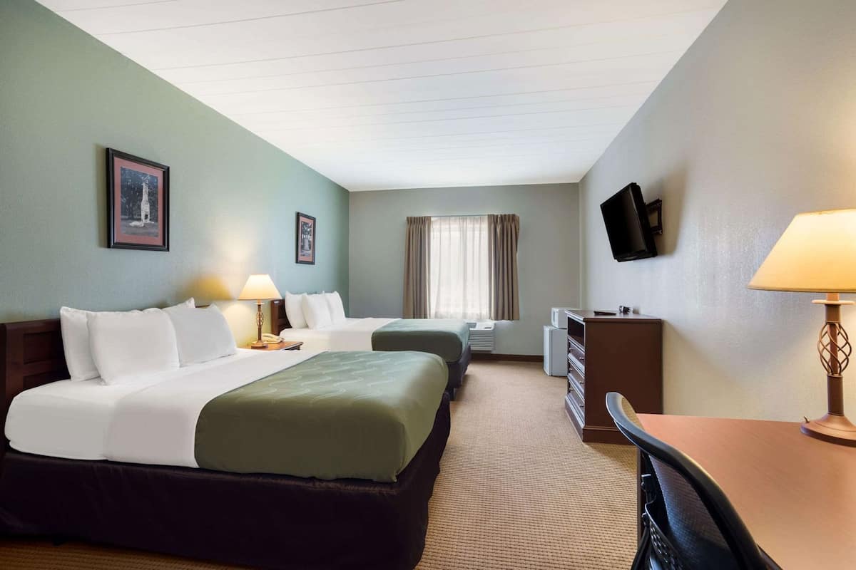 A hotel room with two beds, a desk, a chair, a TV, and a window with curtains.