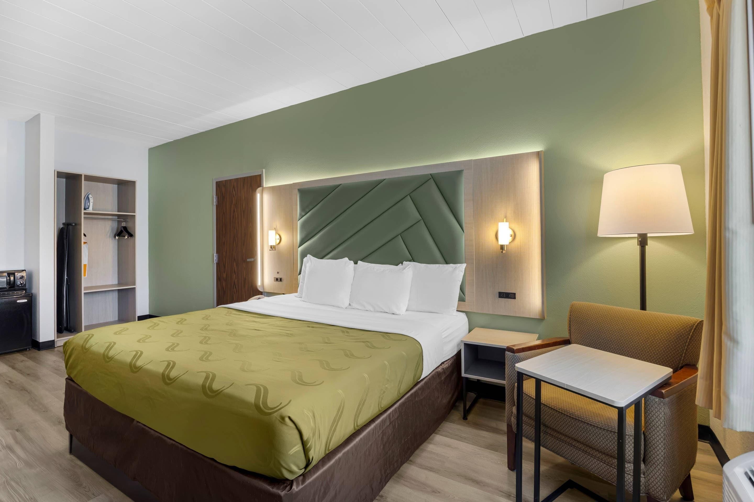 Hotellihuone, jossa on sänky, yöpöytä, tuoli ja vaatekaappi.