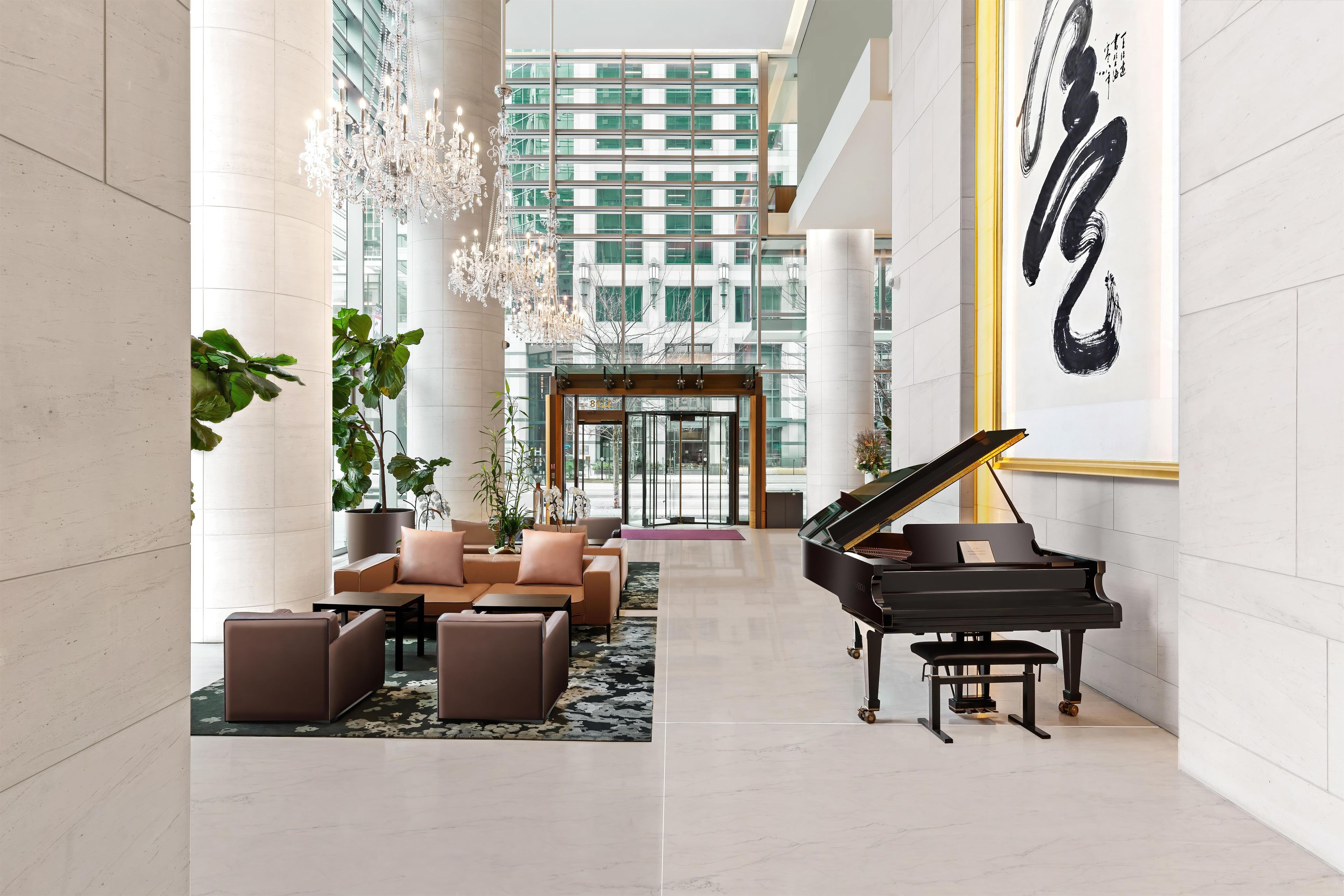 Eine geräumige Lobby mit einem Flügel, bequemen Sitzgelegenheiten, einem Chandelier und einem großen Kunstwerk an der Wand.