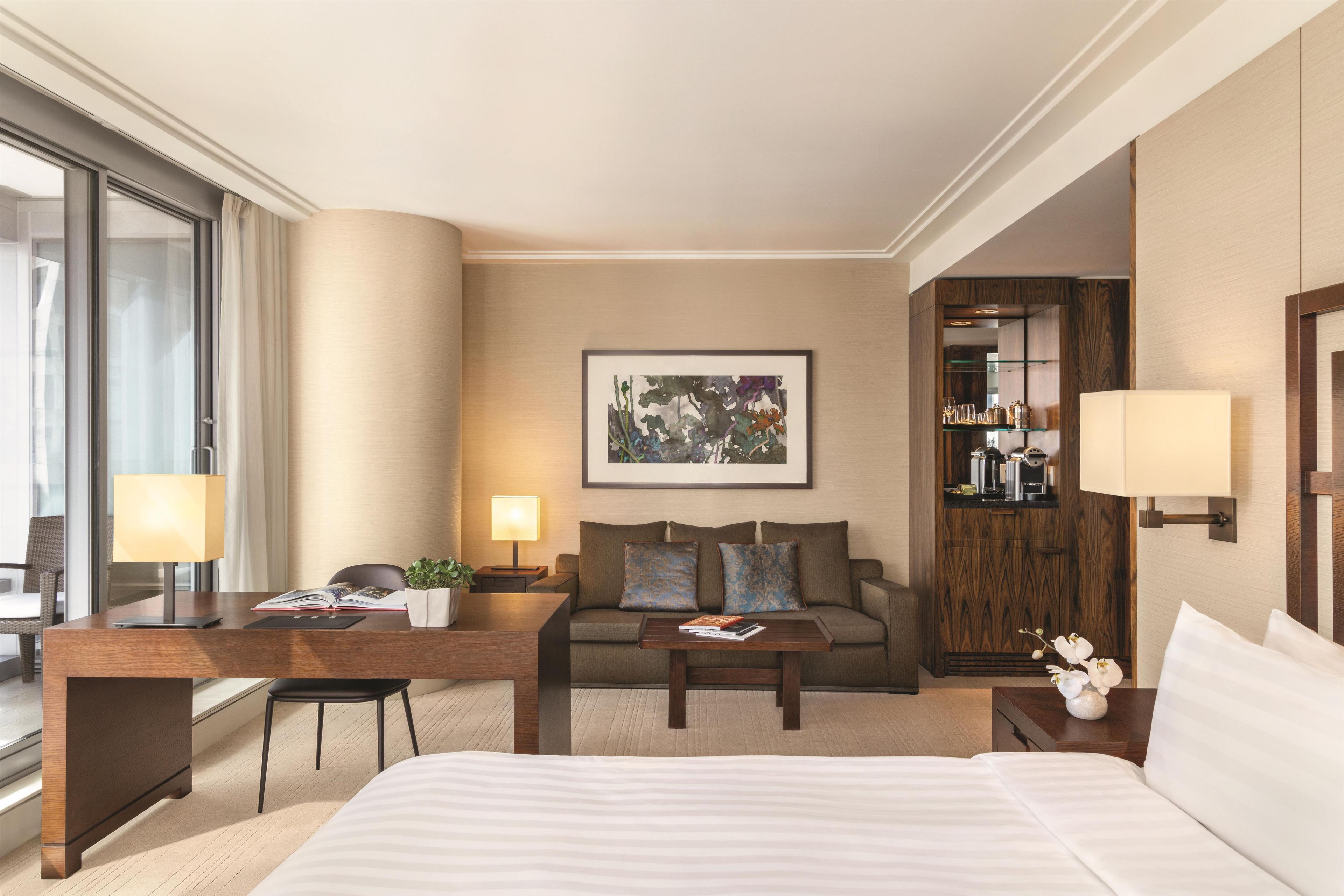 A hotel room with a bed, a desk, a sofa, a coffee table, and a bookshelf.