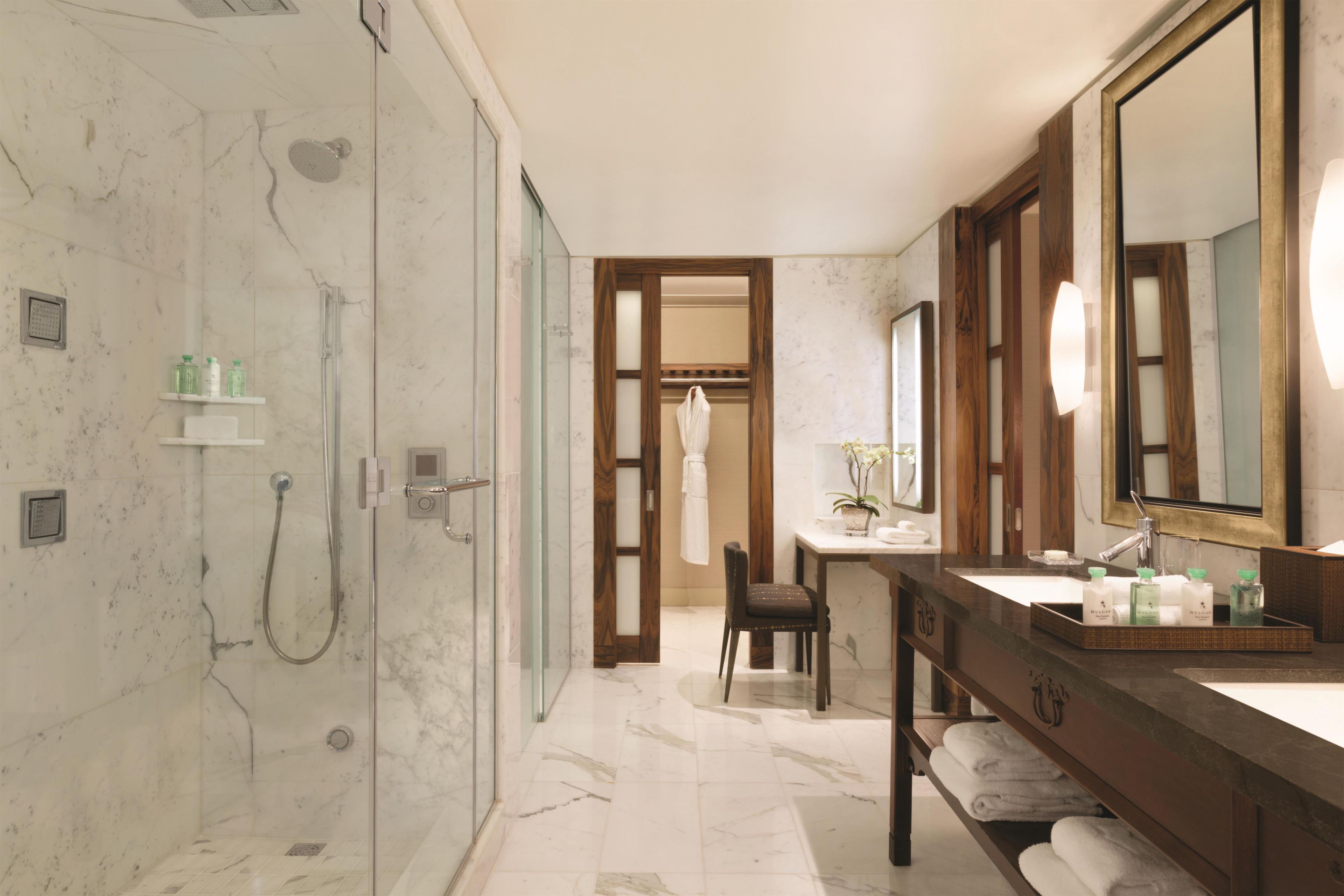 Ein modernes Badezimmer mit einer Glaskabine zur Dusche, einem hölzernen Waschtisch mit großem Spiegel und einer kleinen Sitzecke.
