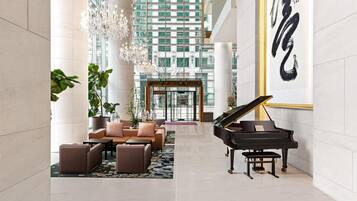 A spacious lobby with a grand piano, comfortable seating, a chandelier, and a large artwork on the wall.