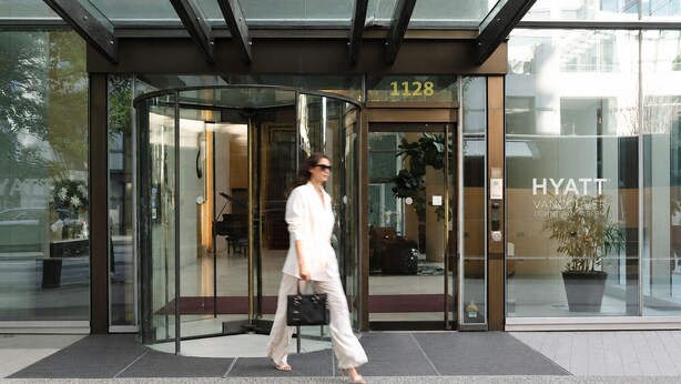Una entrada de hotel moderna con puerta giratoria, fachada de vidrio y una señalización que indica '1128'.