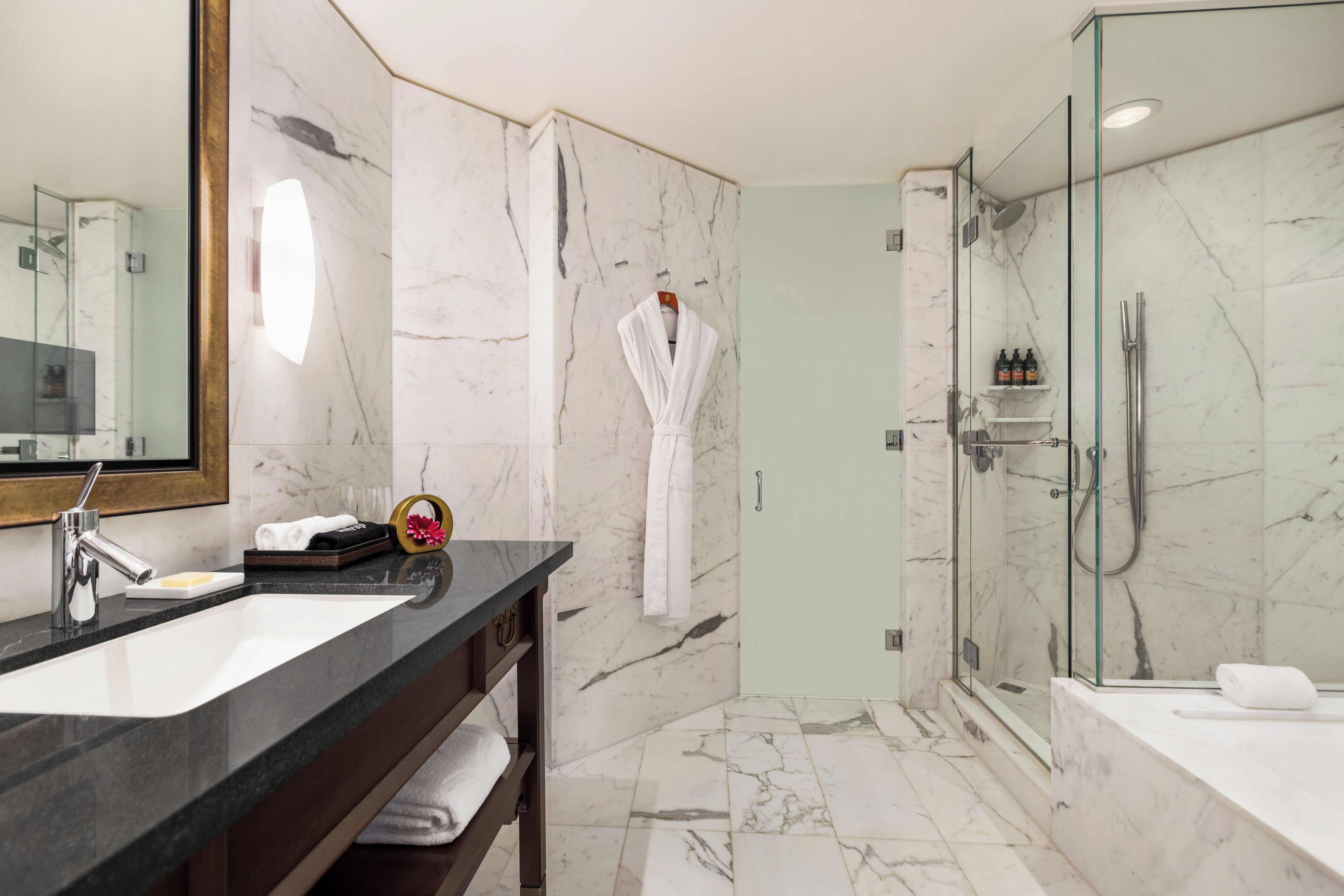 A modern bathroom with a marble sink, a glass-enclosed shower, and a robe hanging on the wall.