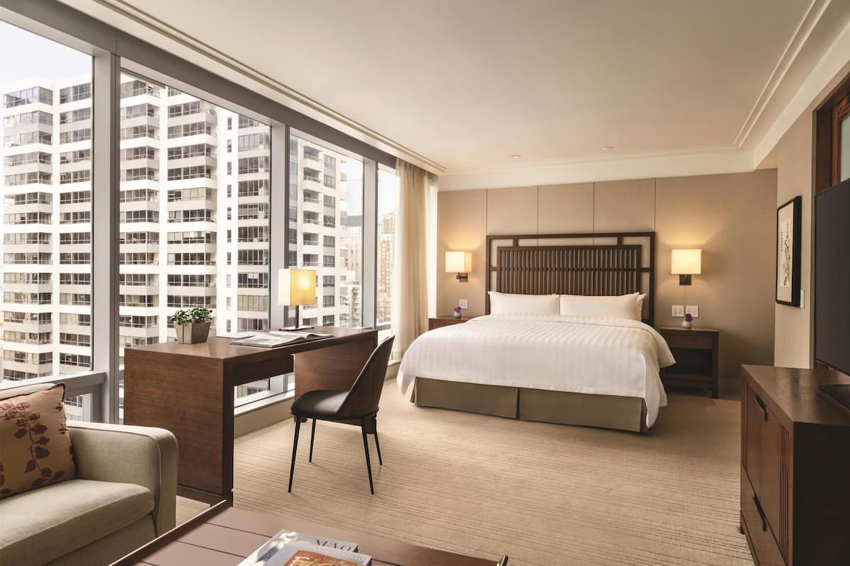 Une chambre d’hôtel avec un grand lit, un bureau, une chaise, une télévision et une vue sur de hauts immeubles.