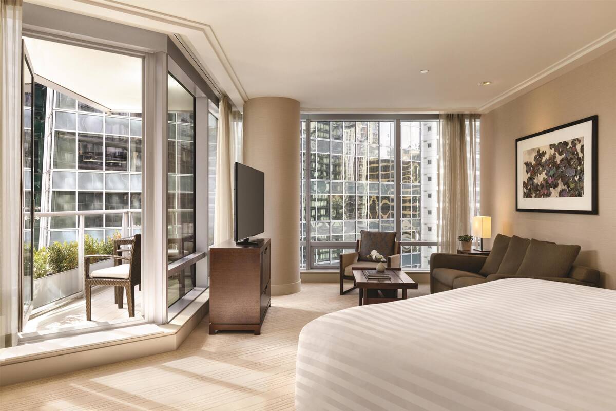 Une chambre d’hôtel moderne dotée d’un grand lit, d’une télévision, d’un canapé, d’un fauteuil et d’un balcon offrant une vue sur la ville.