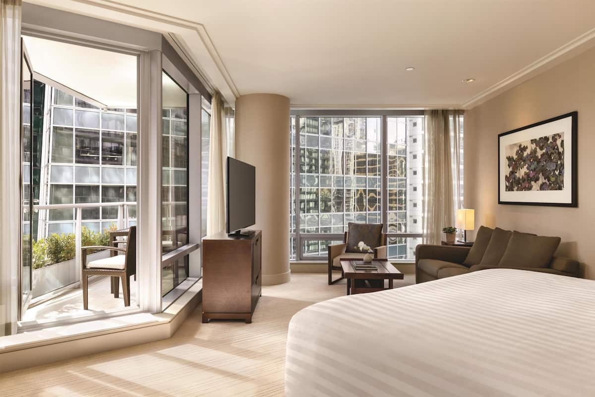 Ein modernes Hotelzimmer mit einem großen Bett, einem Fernseher, einer Couch, einem Sessel und einem Balkon mit Stadtblick.