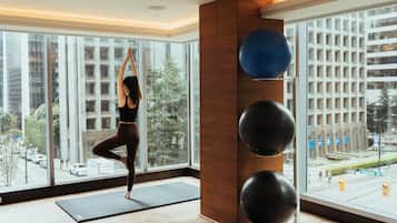 Una colchoneta de yoga en el suelo, una persona en una postura de yoga y pelotas de ejercicio fijadas a la pared.
