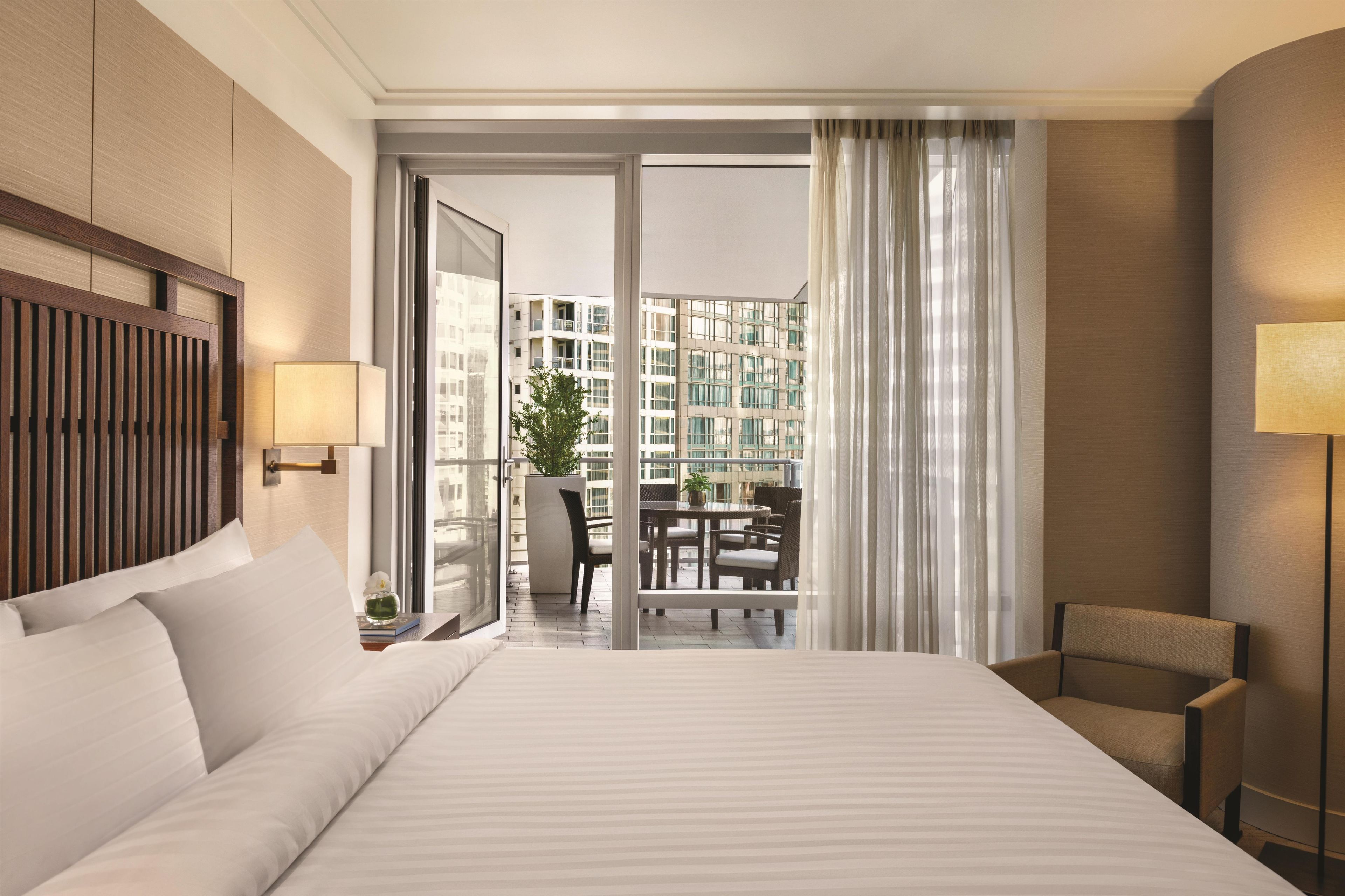 A hotel room with a large bed, a sitting area with a chair, a table, and a balcony with a view of the city.