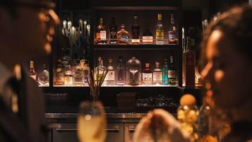 A bar area with shelves of liquor bottles, a hanging lamp, and a person holding a glass.