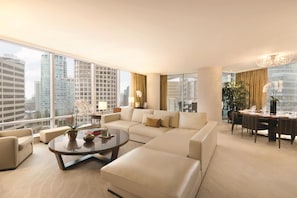 A modern living room with a large sofa, a coffee table, and a dining area with a chandelier.