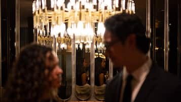 Zona de bar con una araña, asientos de cuero y superficie reflectante.