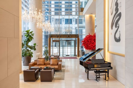Experience the grand piano and comfortable seating in our spacious lobby, surrounded by a large potted plant and natural light.