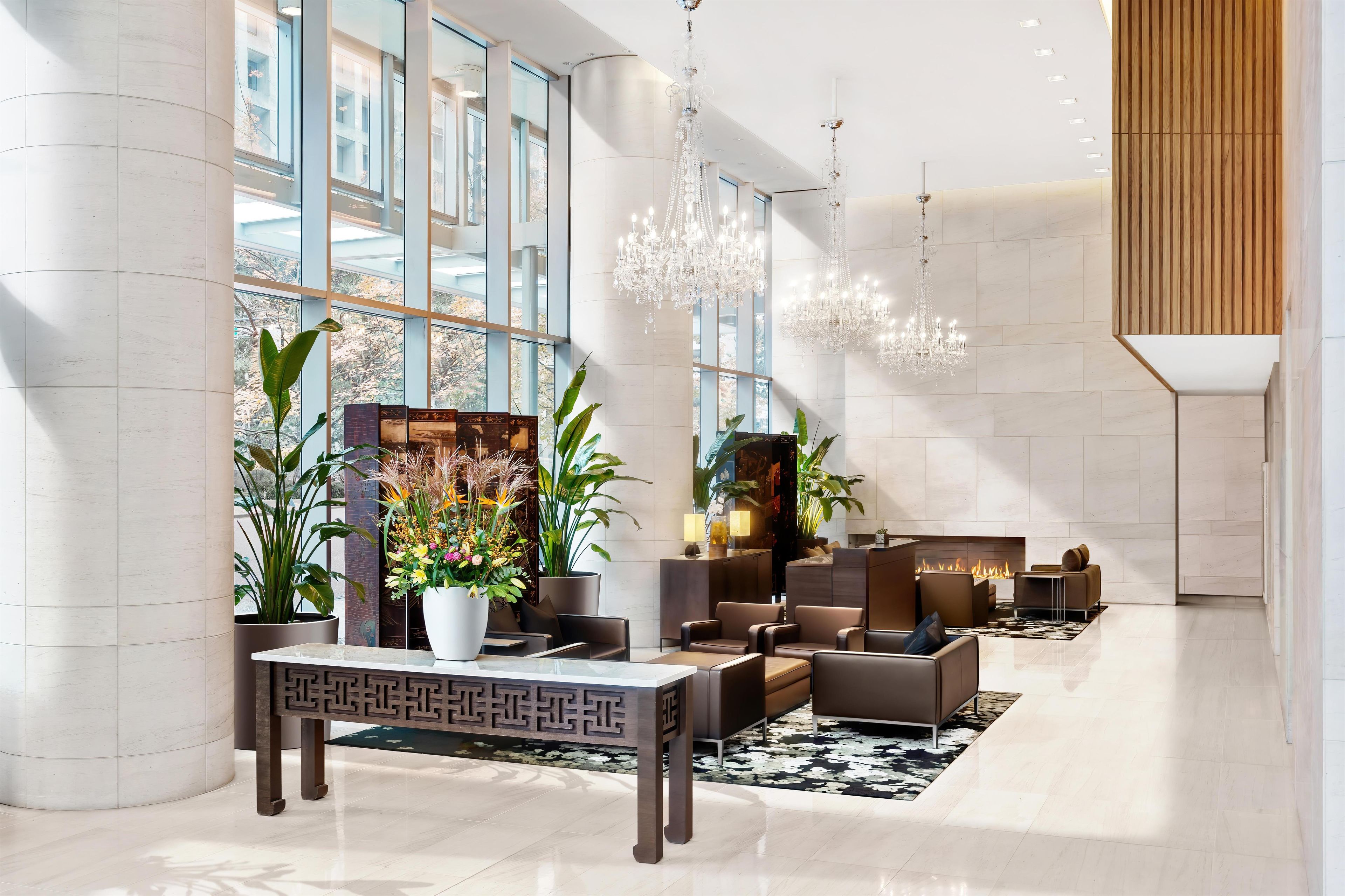 A modern lobby with a reception desk, seating area, large windows, and decorative plants.