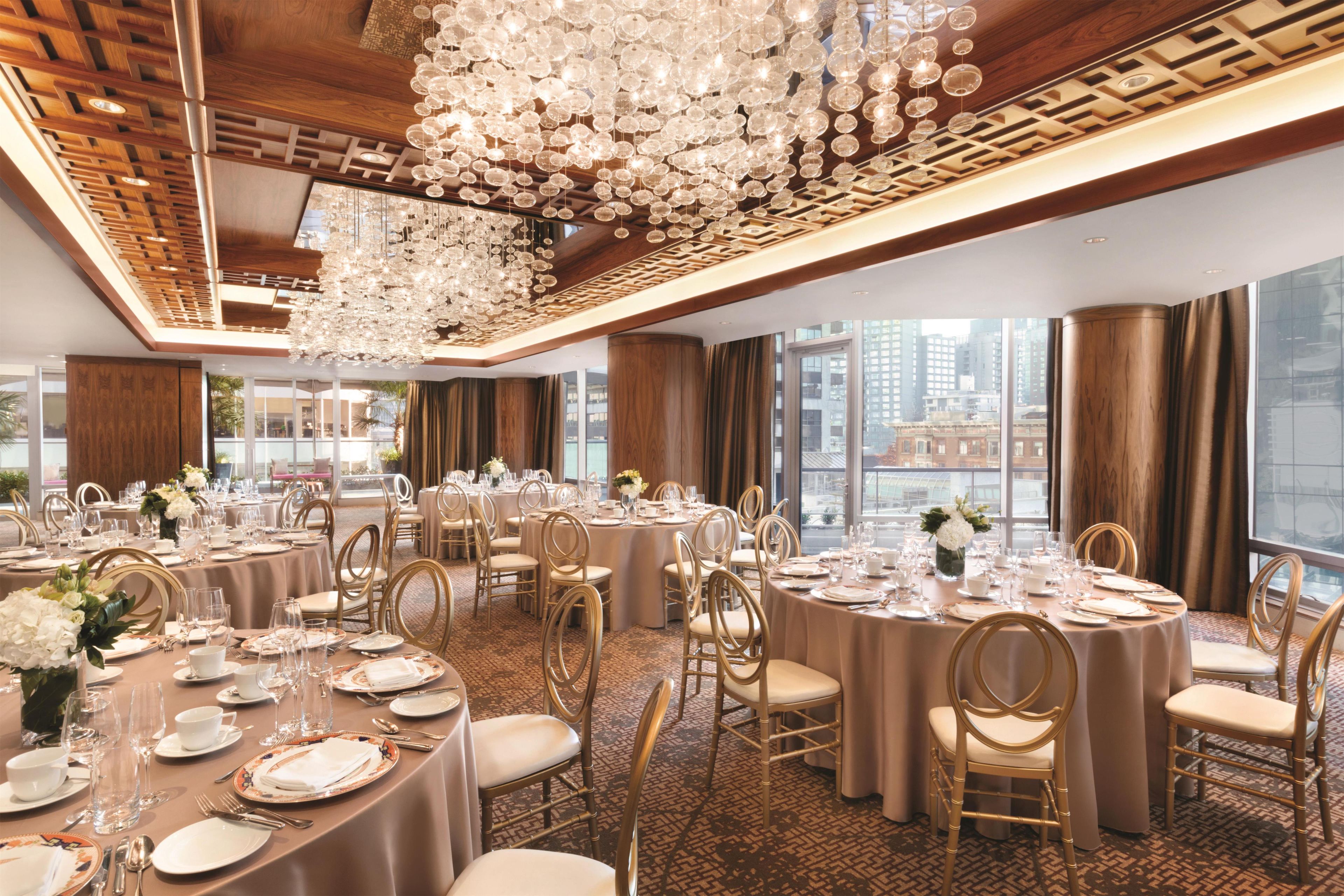 A banquet hall with round tables, gold chairs, and a large chandelier.