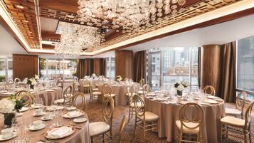A banquet hall with round tables, gold chairs, and a large chandelier.