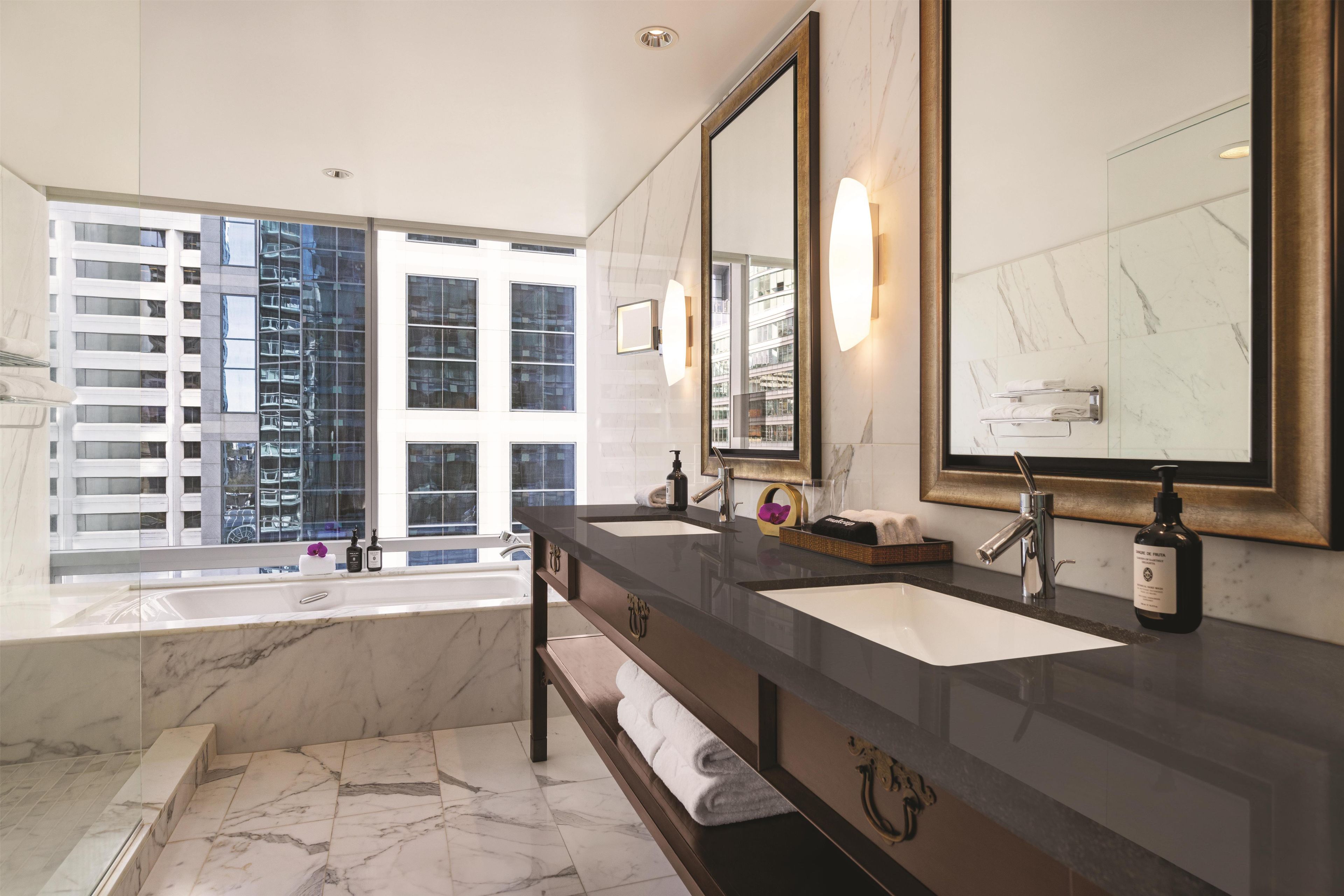 Ein modernes Badezimmer mit großem Fenster, zwei Waschbecken, einer Badewanne und einem Waschtisch mit Spiegel.