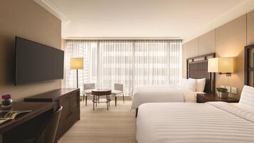 A hotel room with a large bed, a desk with a chair, a TV, and a window with curtains.