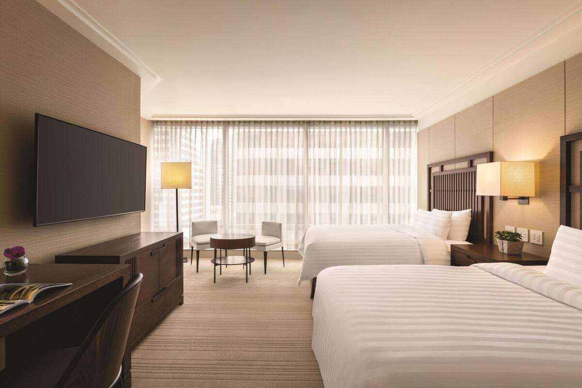 Une chambre d’hôtel avec un grand lit, un bureau avec une chaise, une télévision et une fenêtre avec des rideaux.