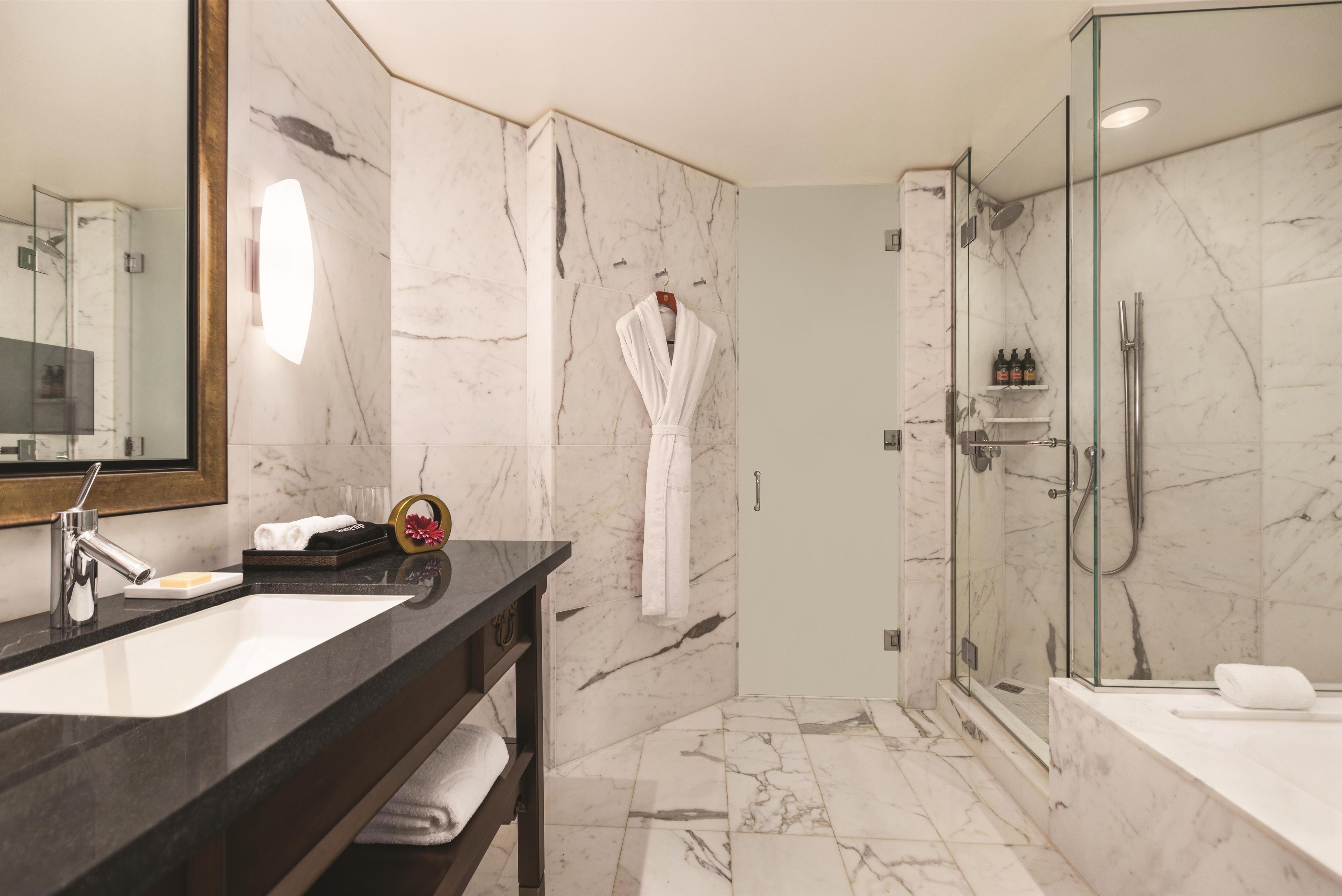 A modern bathroom with a marble vanity, a glass-enclosed shower, and a robe hanging on the wall.