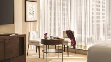 A hotel room with a bed, a desk, a chair, a round table, and a window with sheer curtains.