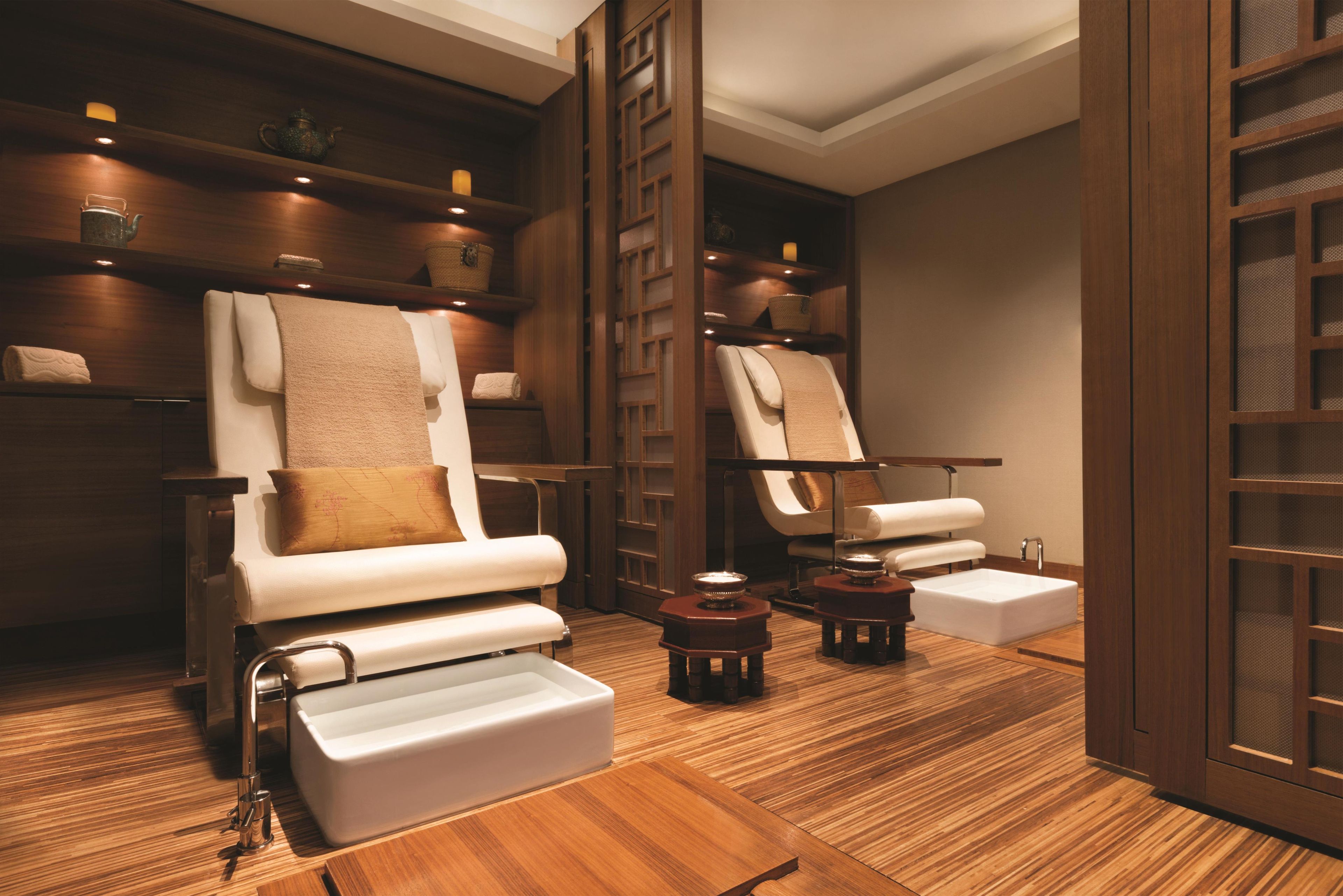 A spa room with two massage chairs, wooden shelves with candles, and a wooden floor.