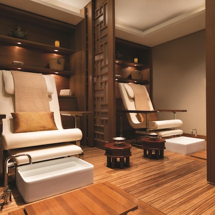 A spa room with two massage chairs, wooden shelves with candles, and a wooden floor.