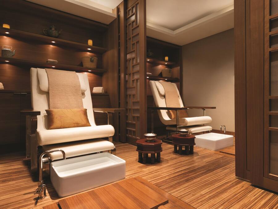 A spa room with two massage chairs, wooden shelves with candles, and a wooden floor.