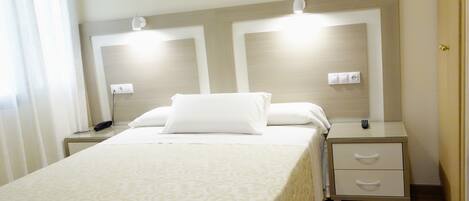 A hotel room with a large bed, two bedside tables, a nightstand, and a wall-mounted light fixture.