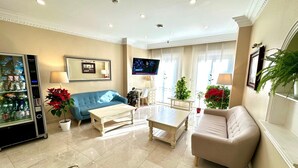 A modern living room with a blue sofa, beige armchairs, a coffee table, and a TV mounted on the wall. - Hostal Toledo (Toledo)