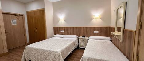 A hotel room with two single beds, wooden headboards, a wooden wardrobe, and a mirror.