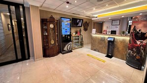 A lobby with a reception desk, a digital information kiosk, a large wall clock, and a decorative wall panel. - Hostal Toledo (Toledo)