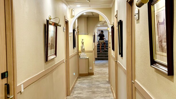 A hotel hallway with framed artwork on the walls, a statue in the center, and a staircase leading to another floor. - Hostal Toledo (Toledo)
