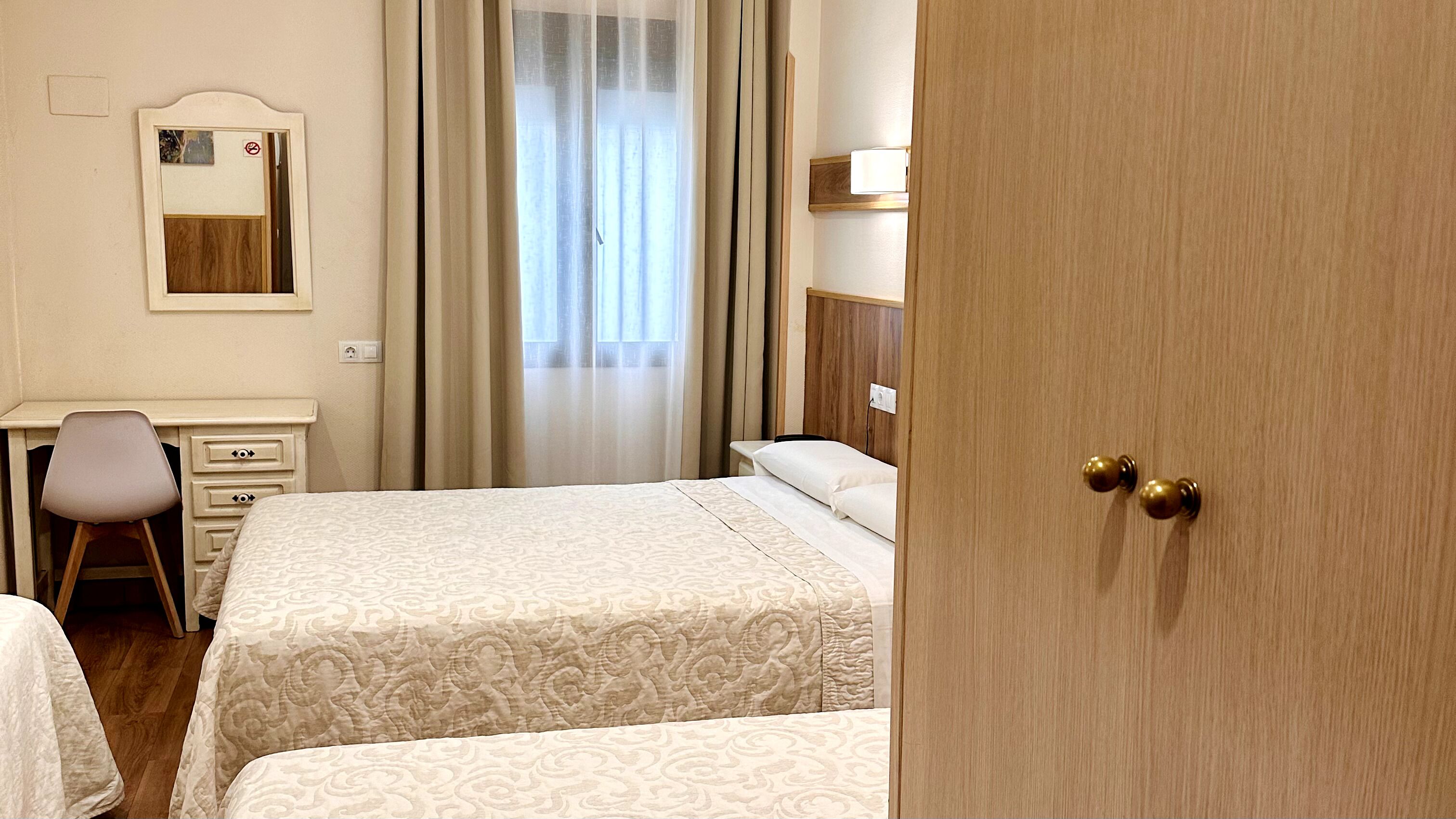 A hotel room with two beds, a desk, a chair, a mirror, and a door.