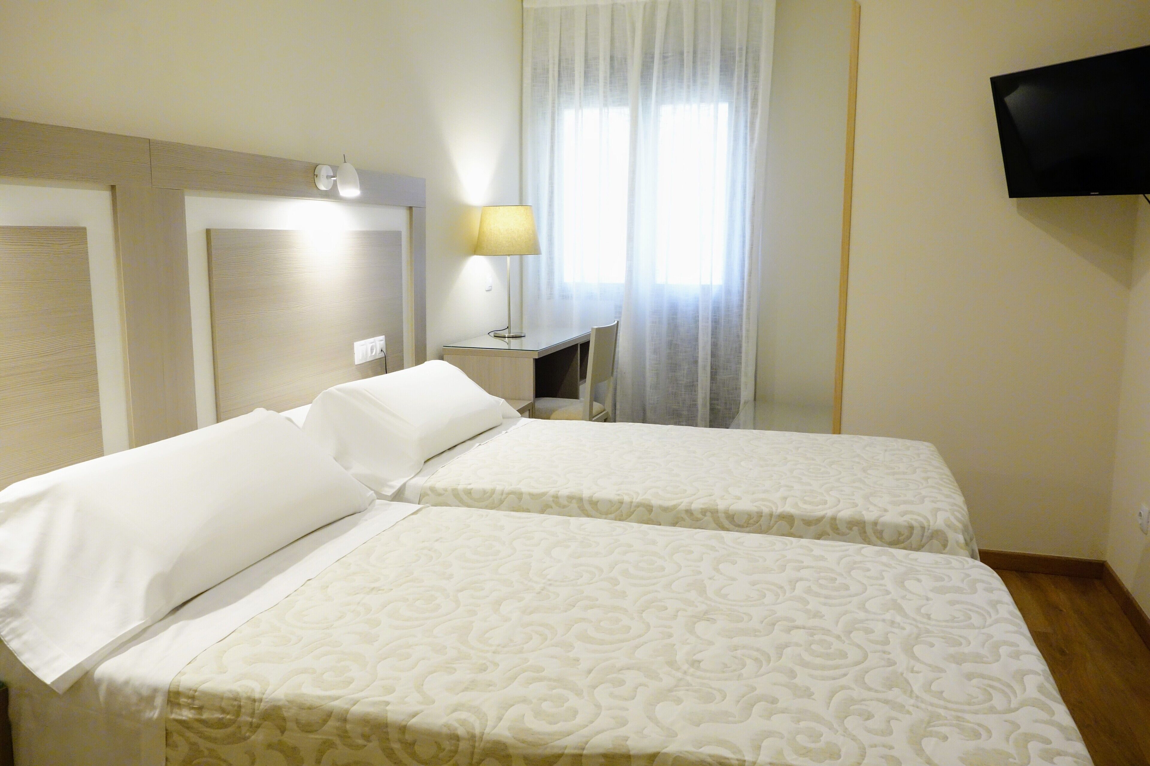 Une chambre d’hôtel avec deux lits, un bureau, une lampe, une télévision et une fenêtre avec des rideaux.