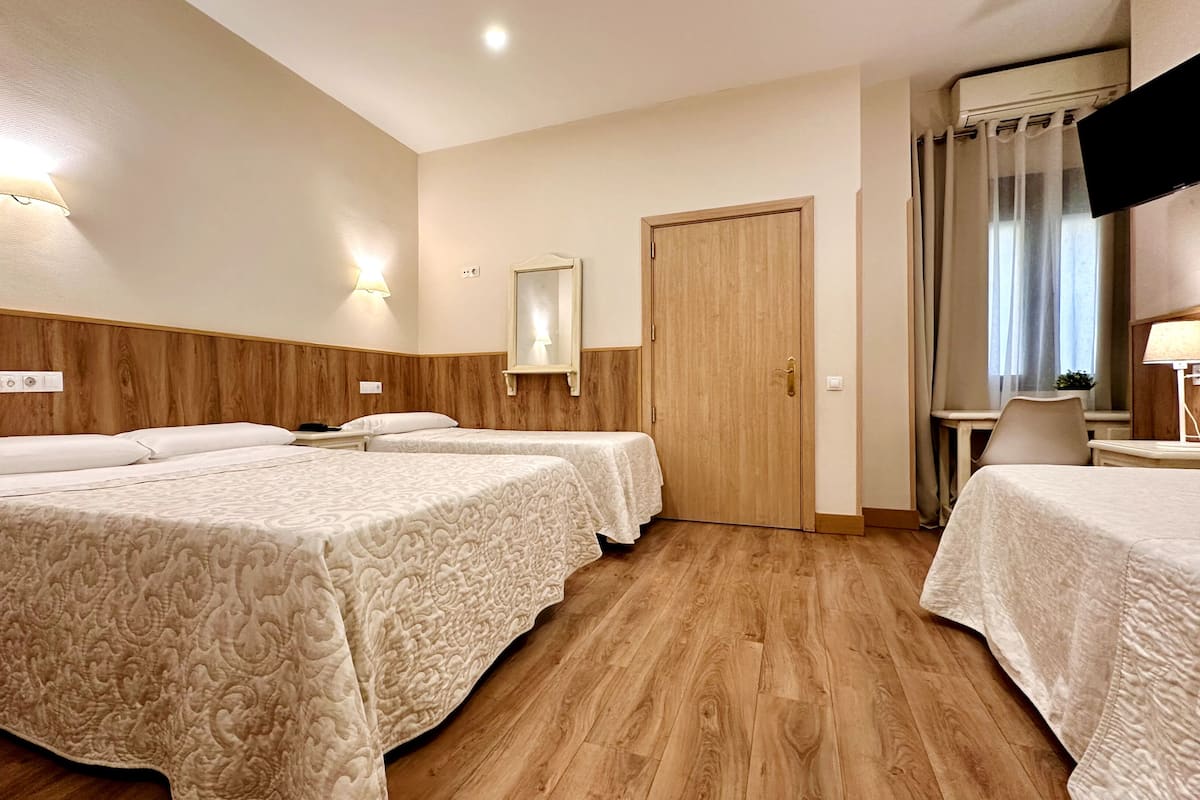 A hotel room with two beds, wooden headboard, a wooden door, a small table with a lamp, and a mirror on the wall.