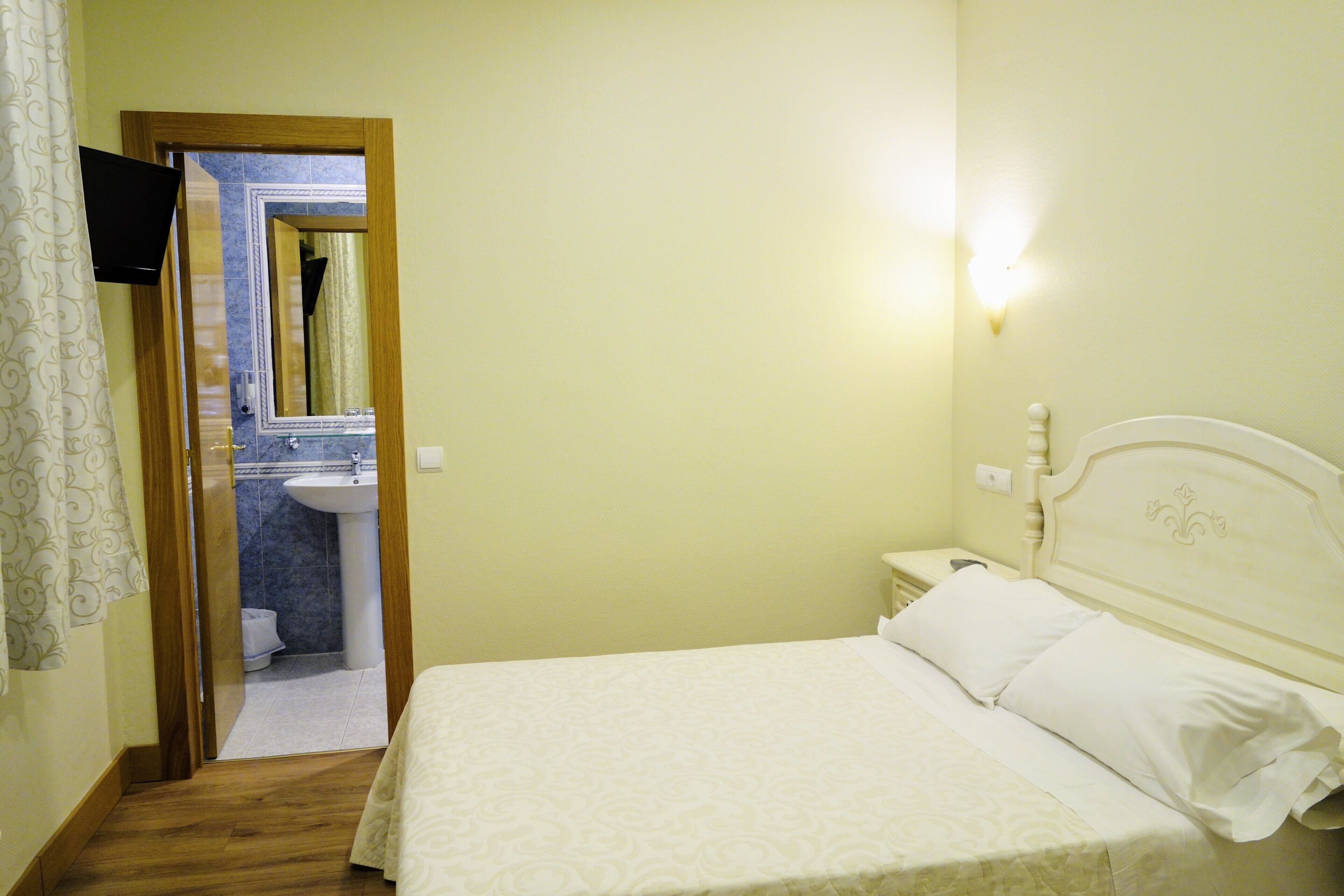 Ein Schlafzimmer mit einem Bett, einem Nachttisch, einer Wandleuchte und einem durch eine geöffnete Tür einsehbaren Badezimmer.