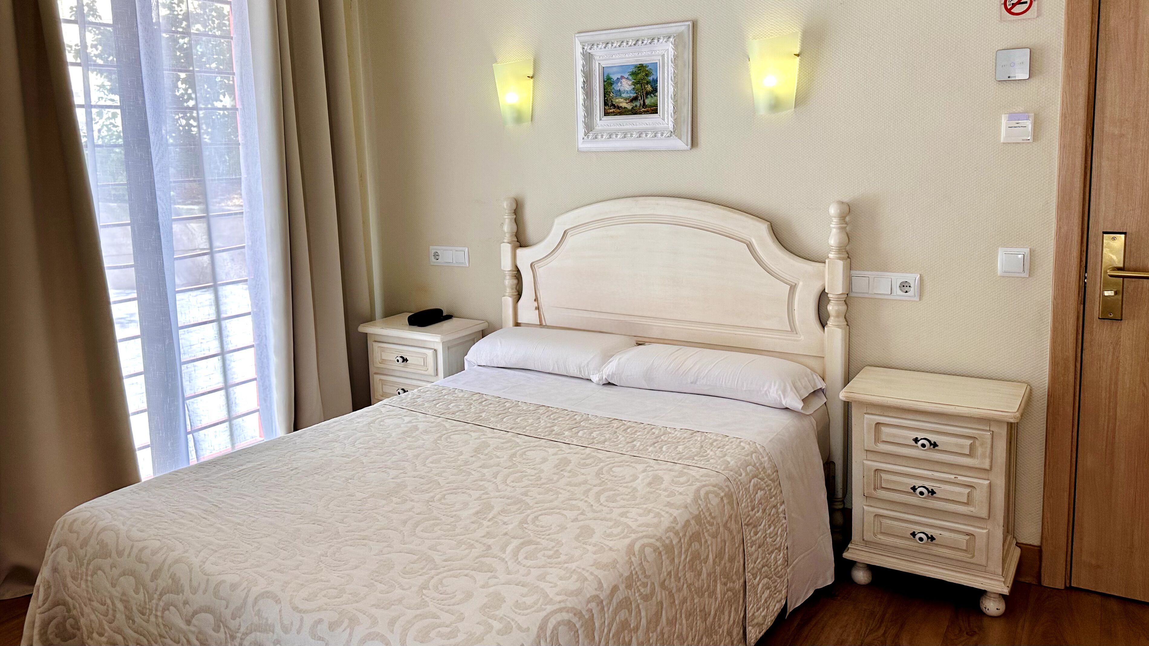 A neatly arranged bedroom with a large bed, bedside tables, a nightstand, and a wall-mounted light fixture.