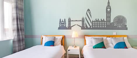 A hotel room with two beds, a nightstand with a lamp, and a wall mural of London landmarks.