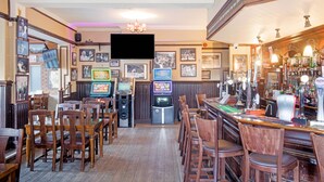 A bar area with wooden chairs, a counter with a cash register, and a television mounted on the wall. - OYO The Green Man Pub and Hotel (Wembley)