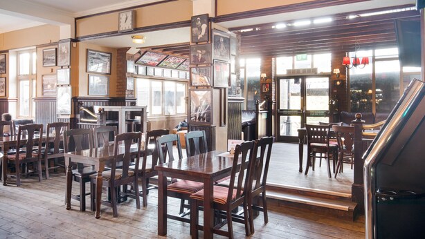A restaurant with wooden tables and chairs, a piano, and framed pictures on the walls. - OYO The Green Man Pub and Hotel (Wembley)