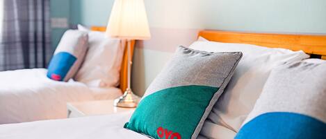 A hotel room with a bed, pillows, a lamp, and a wall with a cityscape mural.