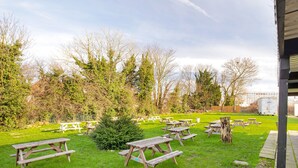 An outdoor picnic area with multiple wooden picnic tables and benches, surrounded by trees and a grassy field. - OYO The Green Man Pub and Hotel (Wembley)