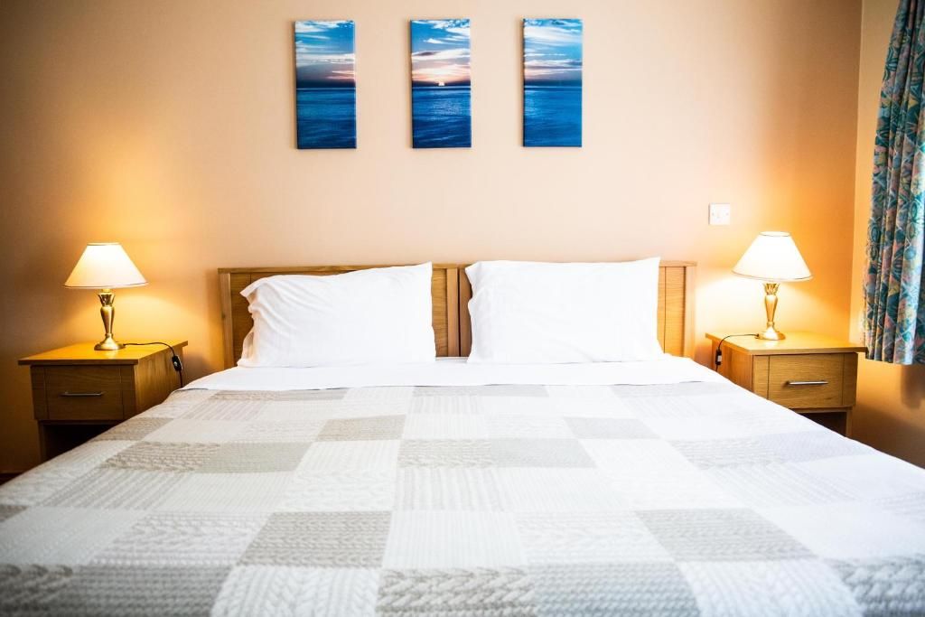 A hotel room with a bed, two bedside tables, and three wall-mounted paintings.