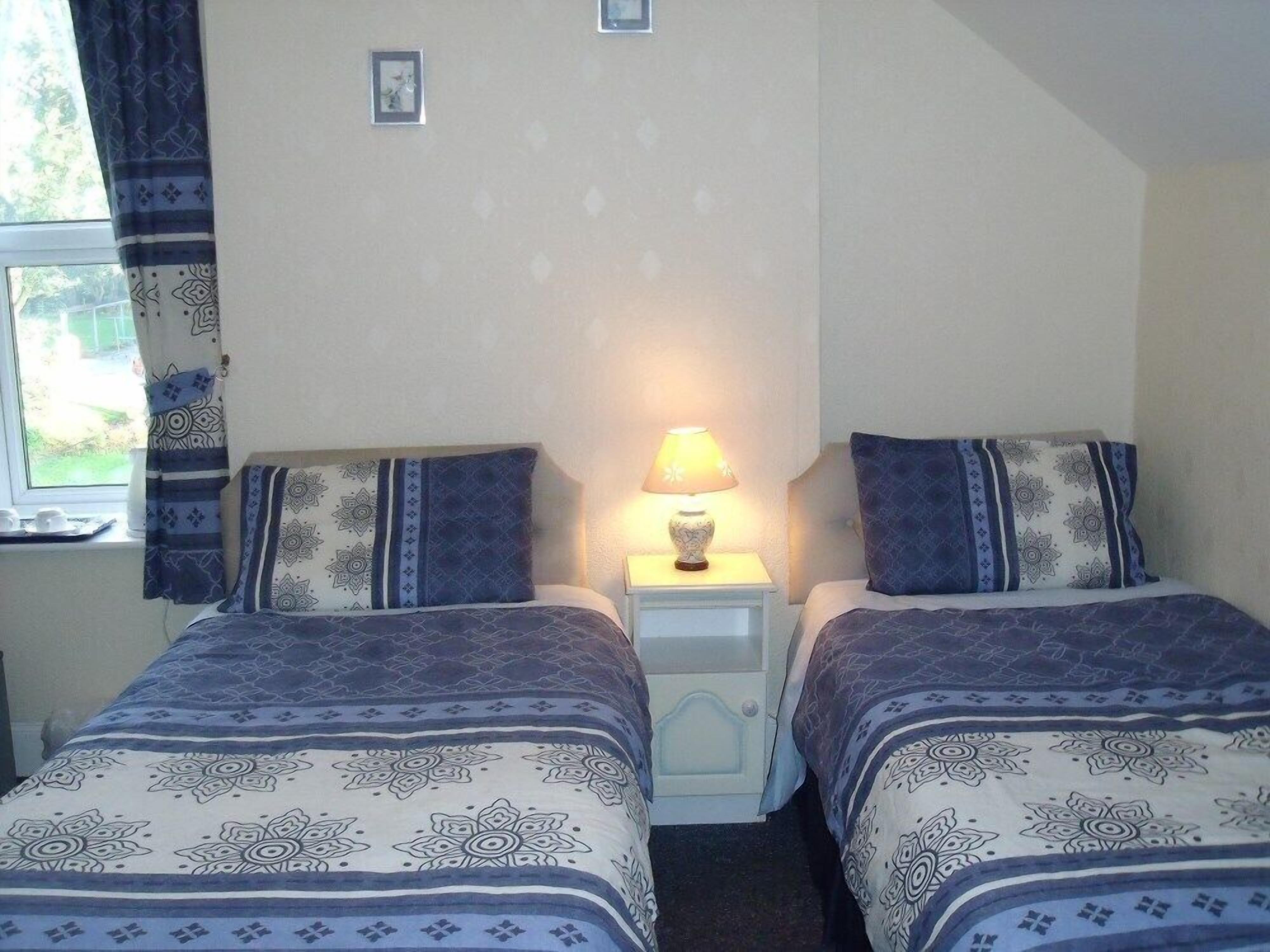 Une chambre avec deux lits, une table de chevet avec une lampe et une fenêtre avec des rideaux.