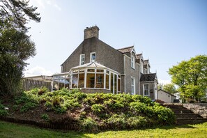 A large house with a prominent bay window, surrounded by lush greenery and a wooden fence. - Groarty House & Manor B&B (Londonderry)