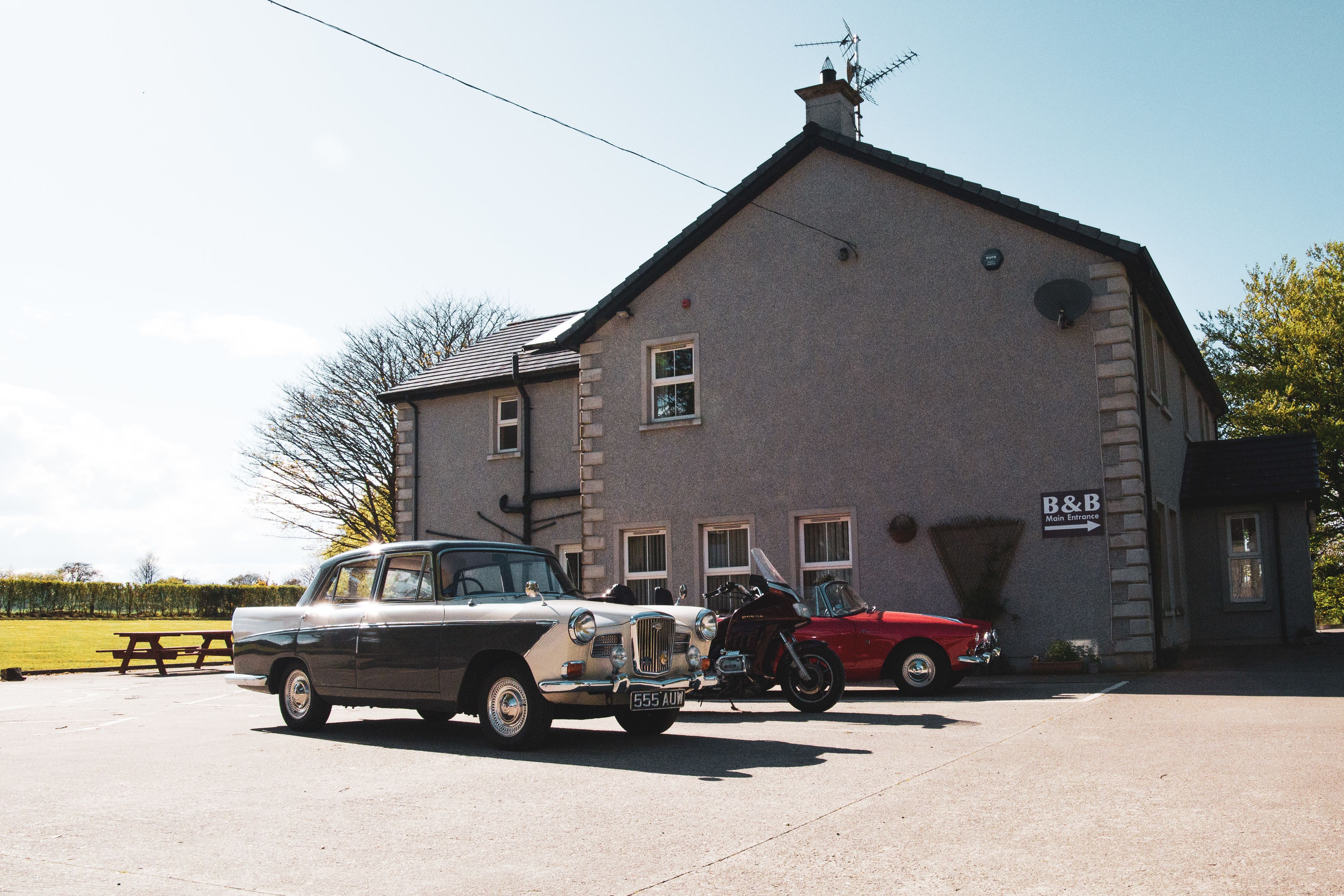 A building with a sign reading "B&B Main Entrance" and a parking area with vintage cars.