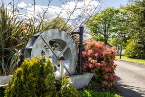 A large water wheel surrounded by lush greenery and flowering plants. - Groarty House & Manor B&B (Londonderry)