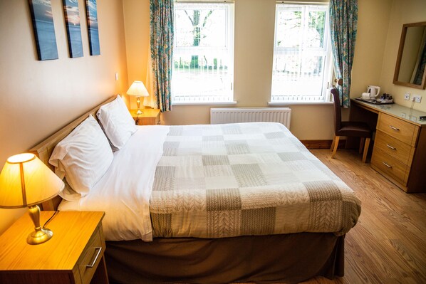 A hotel room with a bed, bedside lamp, desk, chair, and a window with curtains. - Groarty House & Manor B&B (Londonderry)